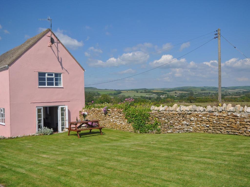 een roze huis met een bank naast een stenen muur bij Cliff Farm No 2 Cottage in Burton Bradstock