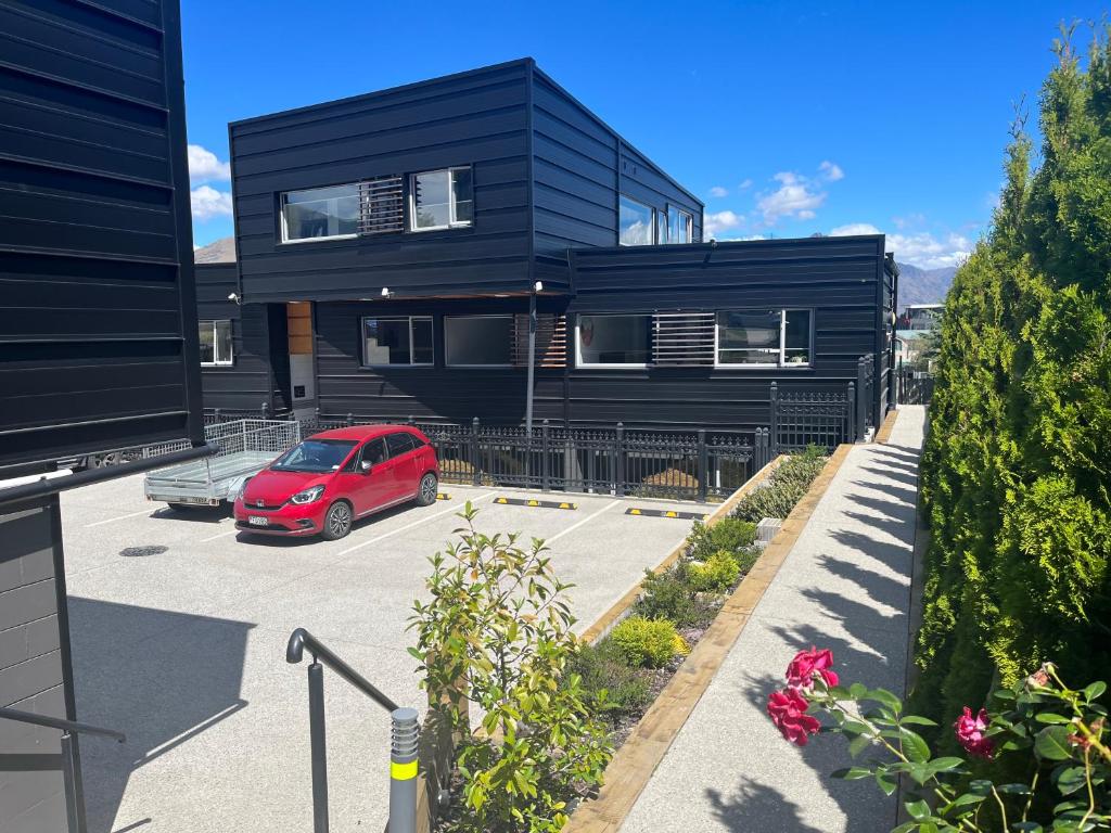a red car parked in a parking lot in front of a black house at Blackrock Apartments Queenstown in Queenstown
