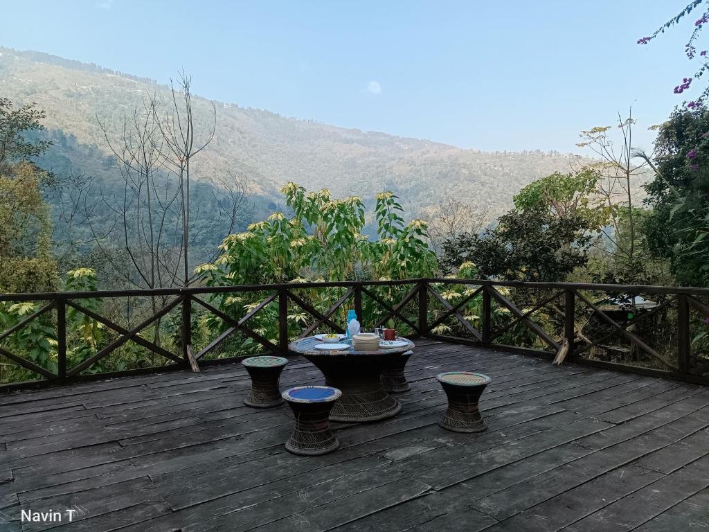 una terraza de madera con mesa y taburetes. en Tathagata Farm en Darjeeling