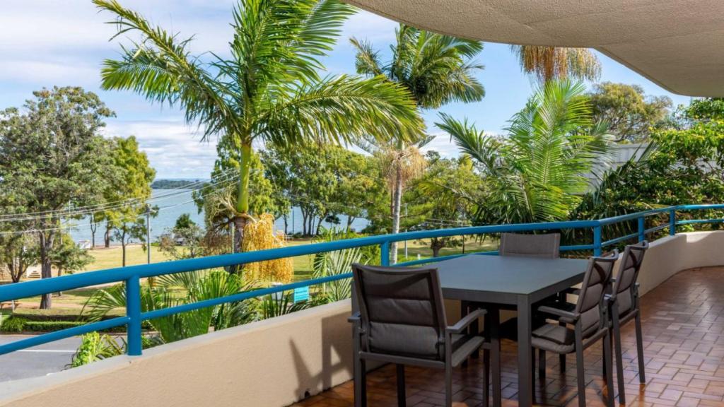 a balcony with a table and chairs and palm trees at Spectacular Waterviews and Sunsets in Bongaree