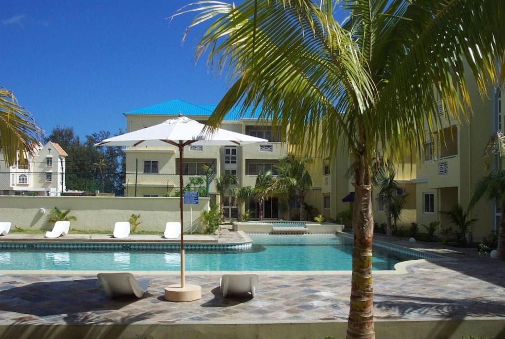 a pool with chairs and an umbrella and a palm tree at Lovely apartment in Flic en Flac, close to the lovely beach and all amenities in Flic-en-Flac