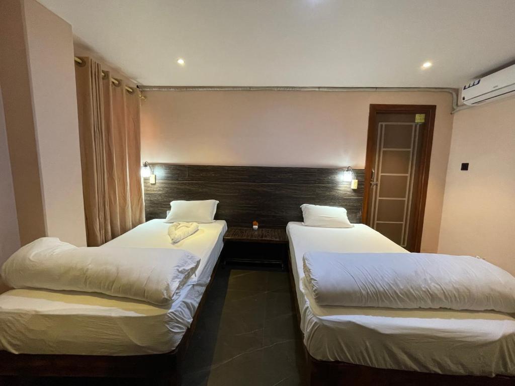 2 camas en una habitación de hotel con sábanas blancas en Hostel The Good Earth Pvt. Ltd., en Pokhara