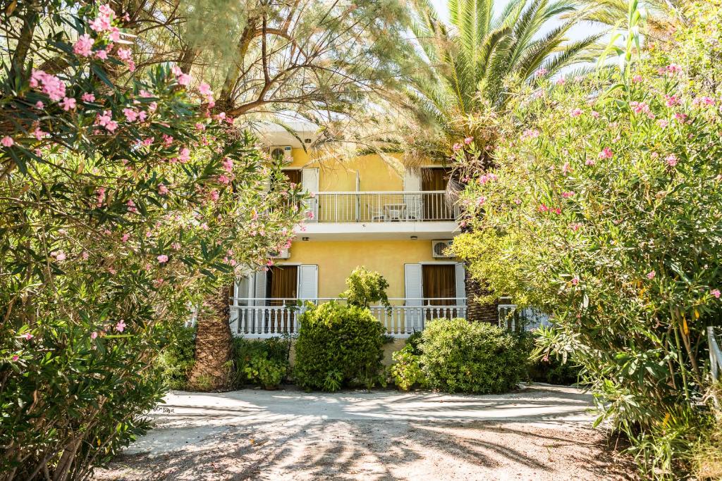 a yellow building with trees and flowers in front of it at Kalofonos Studios in Laganas