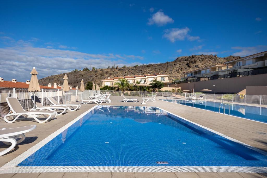 una piscina con sedie e sedie accanto a un edificio di Home2Book Sea View & Design Duplex Los Gigantes a Puerto de Santiago