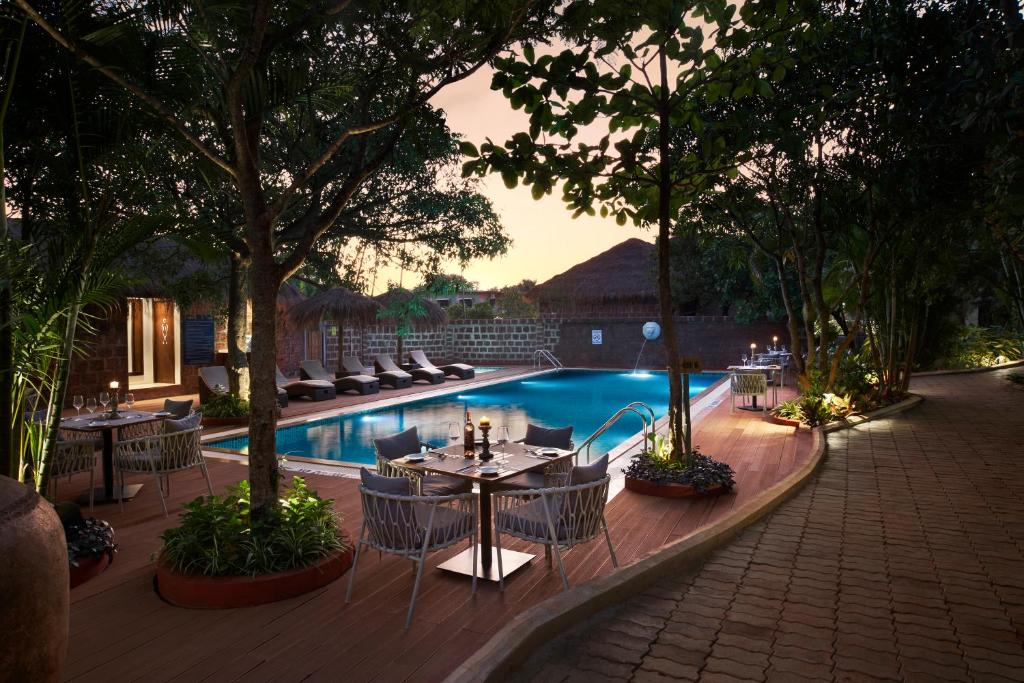 un patio con mesas y sillas junto a una piscina en Larisa Resort Ashwem, en Mandrem