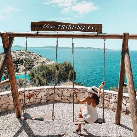 a woman sitting on a swing in front of the ocean at Apartman Lucana in Tribunj