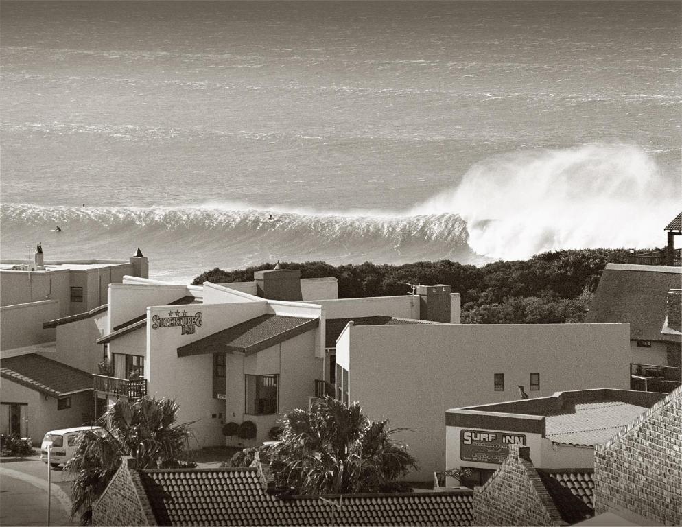a large wave crashing on the ocean with buildings at Supertubes Guesthouse in Jeffreys Bay