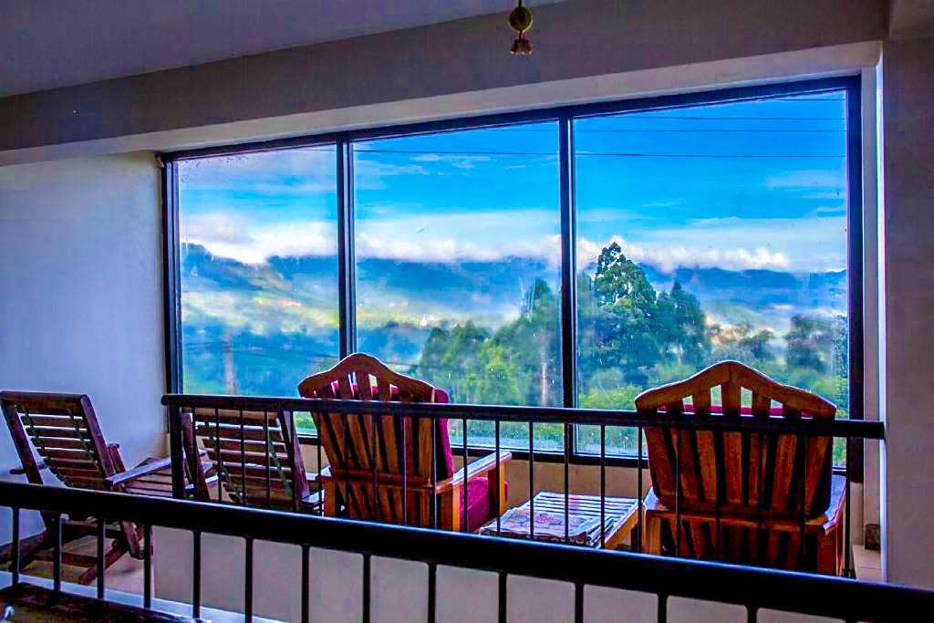 a balcony with three chairs and a large window at Awinco Haputale in Haputale