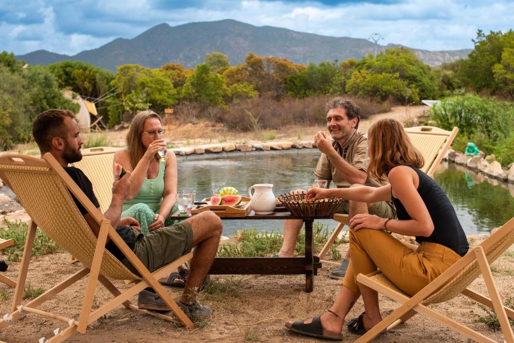 a group of people sitting around a table by a river at ecoVita agri-glamping in San Vito