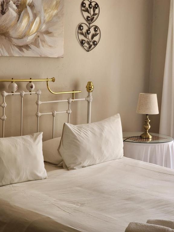 a white bed with white pillows and a table with a lamp at Profcon Resort in Graaff-Reinet