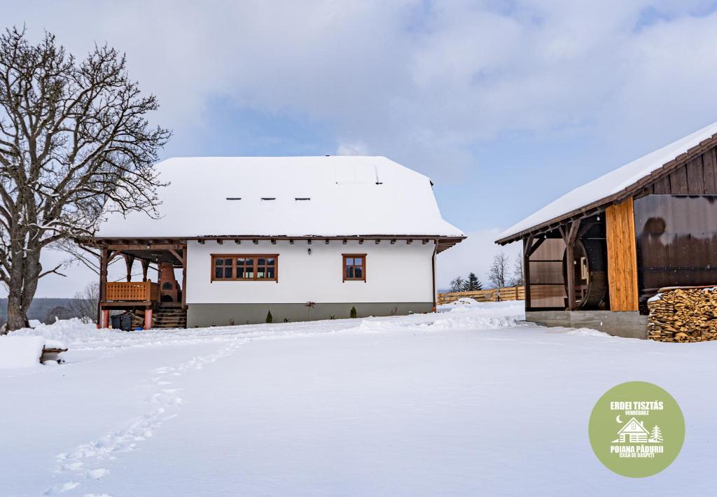 ein Haus mit Schnee auf dem Boden neben einer Scheune in der Unterkunft Poiana Pădurii Casa de Oaspeți in Vărşag