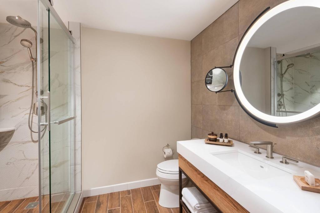 a bathroom with a shower and a sink and a mirror at The Ben, Autograph Collection in West Palm Beach