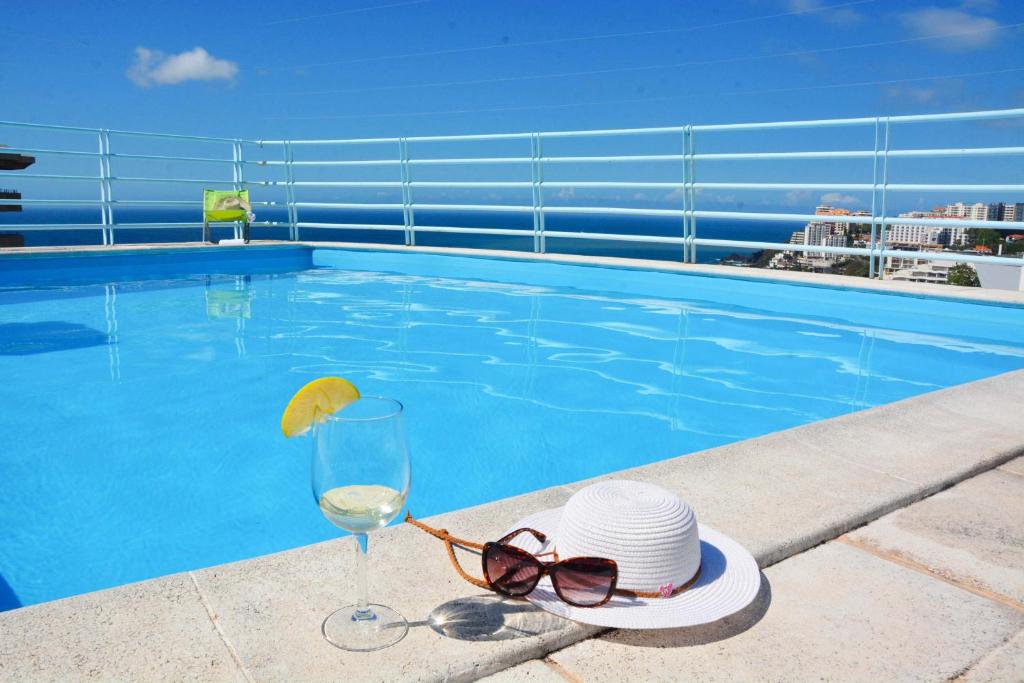 een glas wijn en een hoed en zonnebril naast een zwembad bij Sol do Lido 2 in Funchal