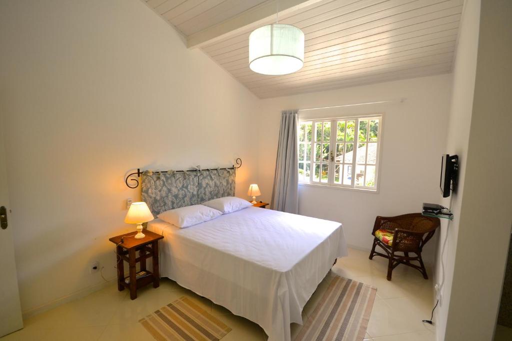 a bedroom with a white bed and a window at Vila da Sol Itaipava casas e estúdios in Itaipava
