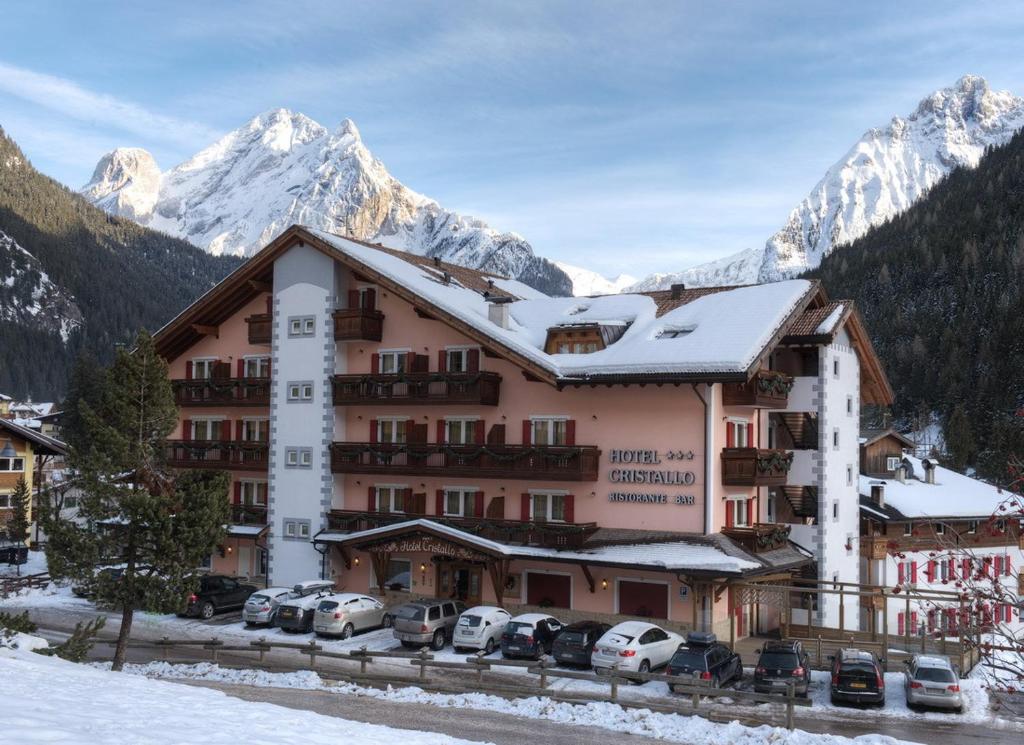 un grande edificio con macchine parcheggiate di fronte di Hotel Cristallo a Canazei