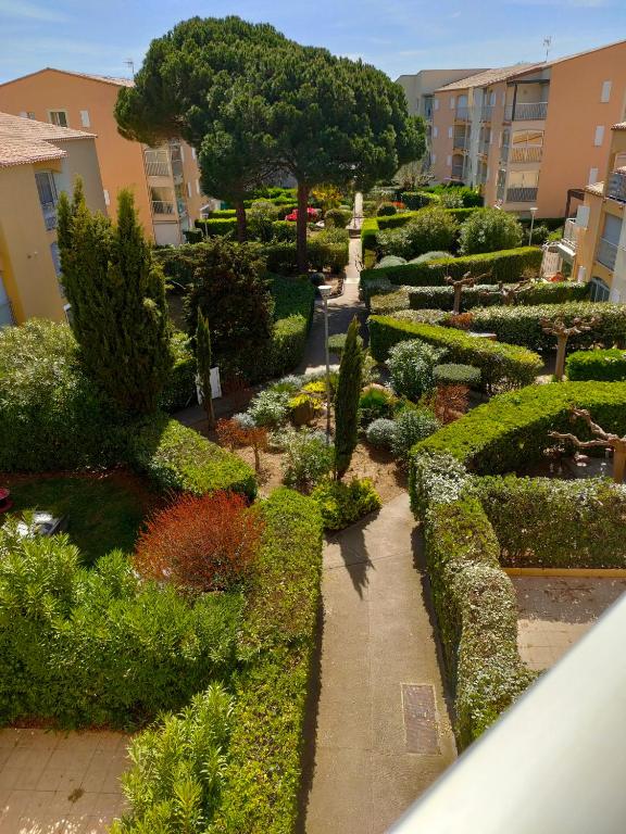 un jardin avec des buissons et des arbres et une passerelle dans l'établissement JEAN BART III Joli 2 pièces cabine mezzanine Richelieu Cap d'Agde, au Cap d'Agde