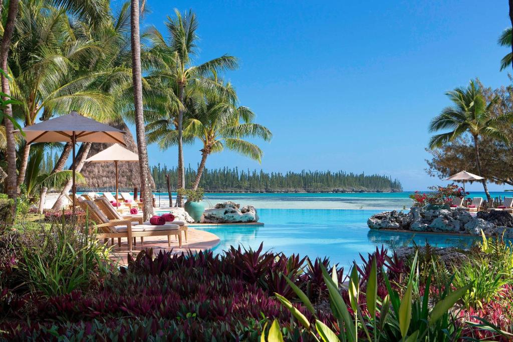 um resort com uma piscina com cadeiras e palmeiras em Le Méridien Ile des Pins em Oro Bay