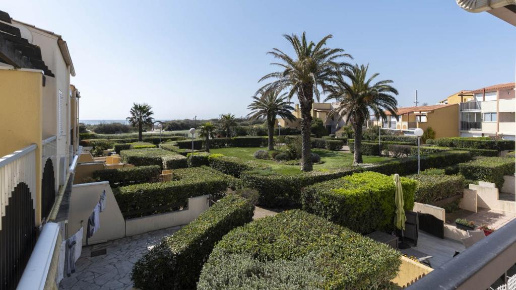 un jardin avec des buissons et des palmiers dans un bâtiment dans l'établissement Aquaplage- 126- Appart vue jardin- 4 pers, au Cap d'Agde