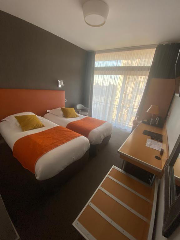 a hotel room with two beds and a desk and a window at Hotel Des Lices in Rennes