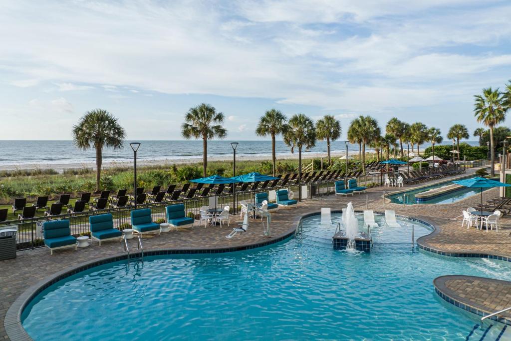 a pool at the beach with chairs and the ocean at Courtyard by Marriott Myrtle Beach Oceanfront in Myrtle Beach