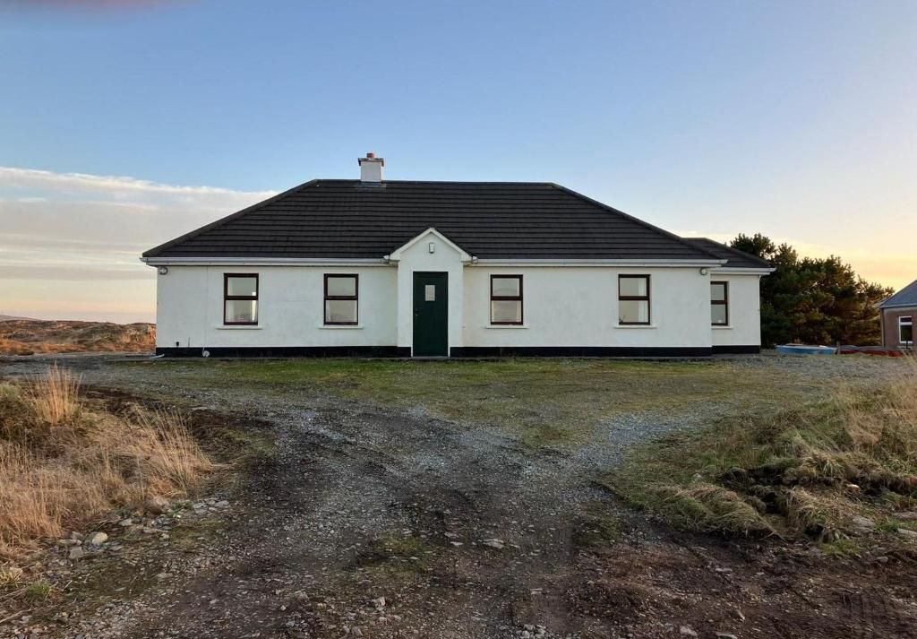 a white house with a black roof on a field at Glynsk Pier Cottage in Carna