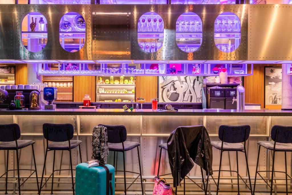 a bar with stools in a restaurant with purple lights at Moxy Berlin Airport in Schönefeld