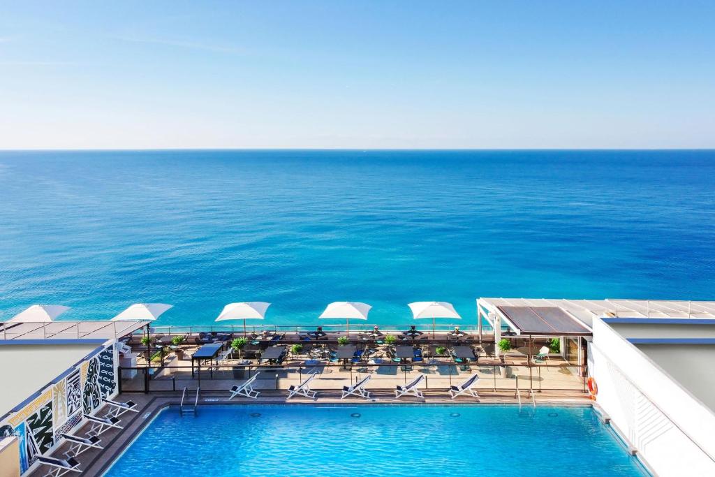 uma piscina com cadeiras e guarda-sóis e o oceano em Le Meridien Nice em Nice