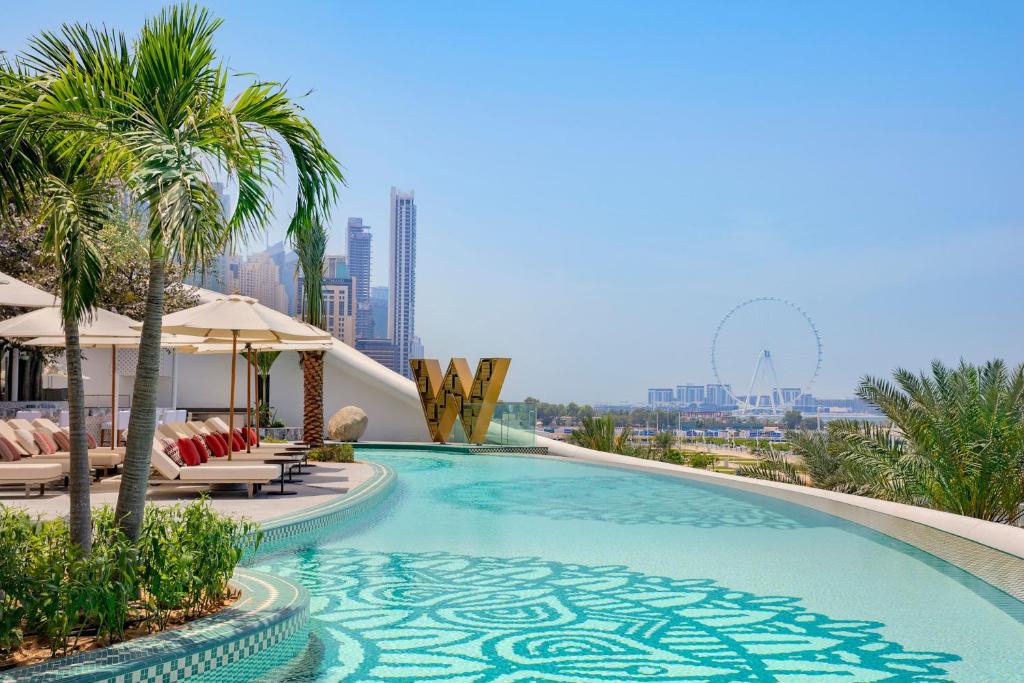 a swimming pool with chairs and palm trees on a building at W Dubai - Mina Seyahi, Adults Only in Dubai