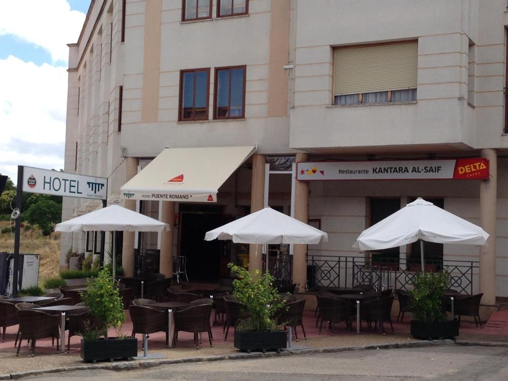 ein Restaurant mit Tischen und Sonnenschirmen vor einem Gebäude in der Unterkunft Hotel Puente Romano in Alcántara