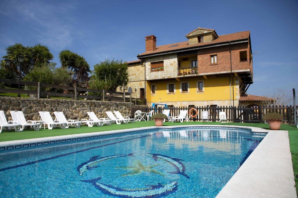 a swimming pool with chairs and a house in the background at Apartamentos La Gloria in Santillana del Mar