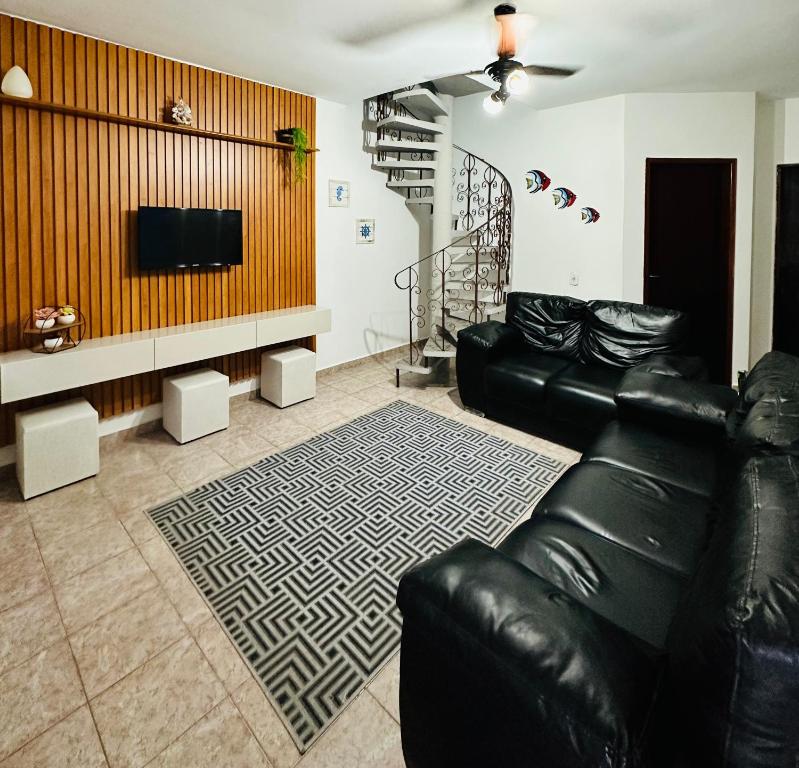 sala de estar con sofá de cuero negro y TV en Casa em frente ao mar - Condominio, en Caraguatatuba
