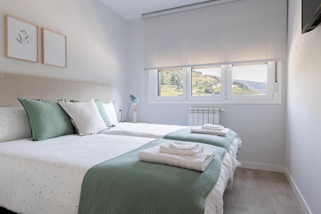 a white bedroom with two beds with towels on them at Apartamentos Nature in Cangas del Narcea