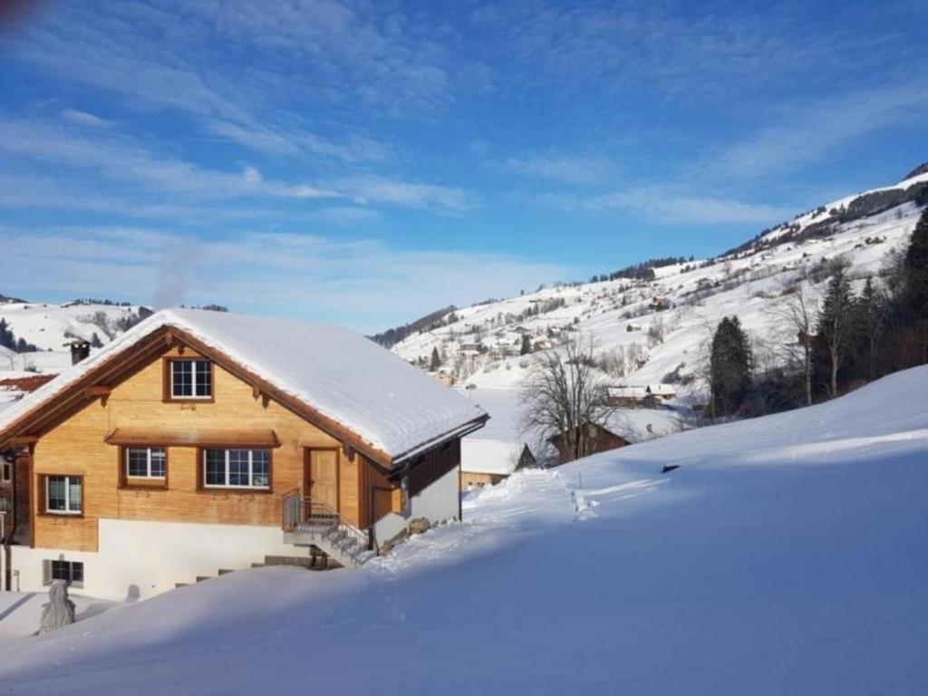 eine Holzhütte im Schnee mit schneebedeckten Bergen in der Unterkunft Ferien im Gugger - Wohnung Stockberg in Nesslau
