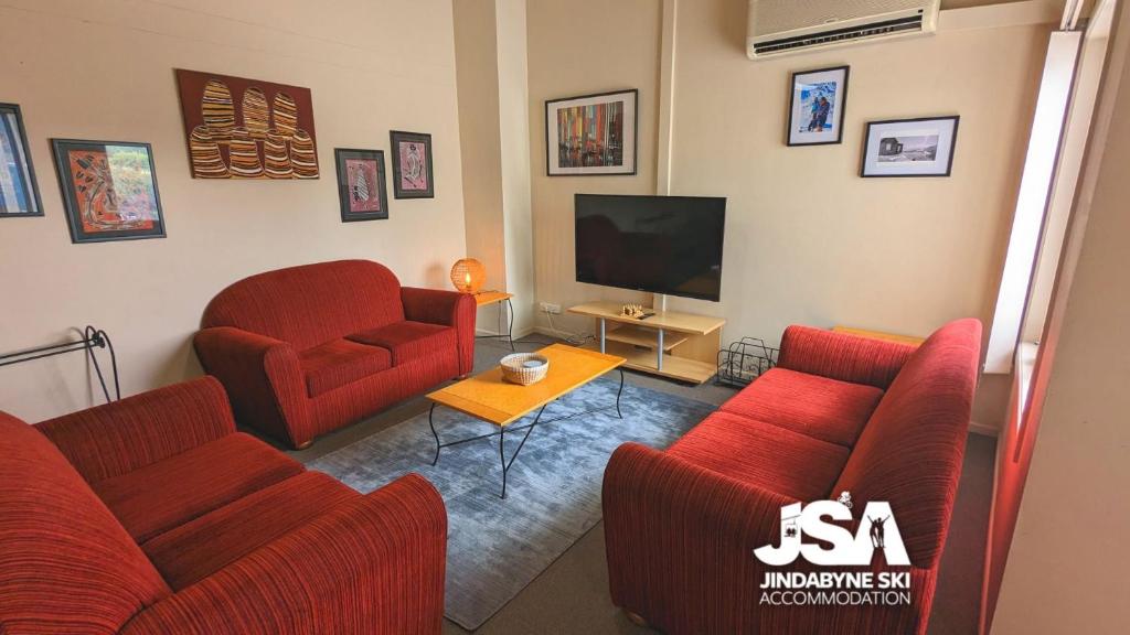 a living room with two red chairs and a television at Razorback 2 in Jindabyne