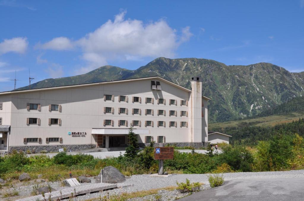 a large white building with mountains in the background at Midagahara Hotel in Tateyama