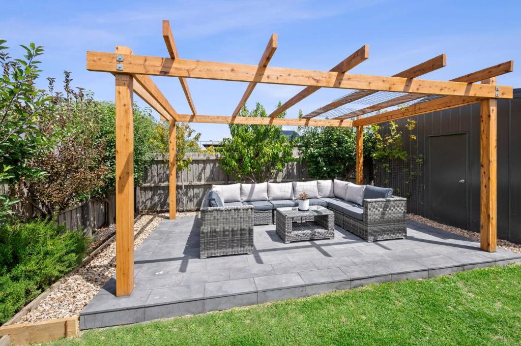 a patio with a wooden pergola and a couch and tables at Aerial Beach House 2 in Torquay