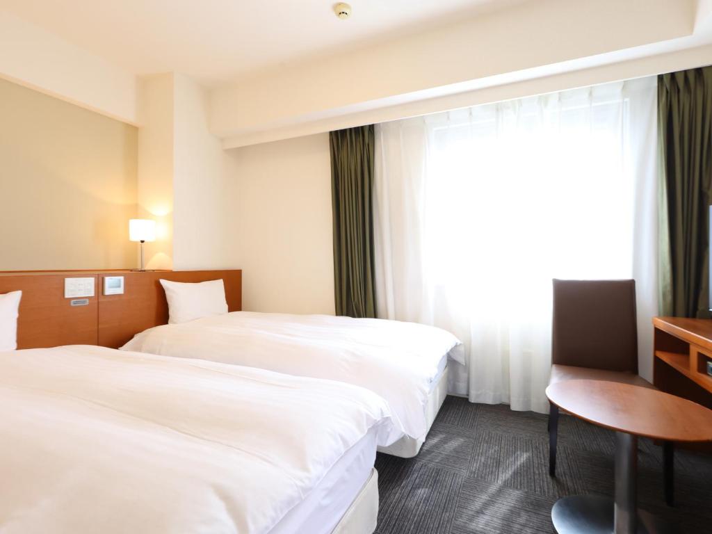 a hotel room with two beds and a table and a window at Dormy Inn Takasaki in Takasaki