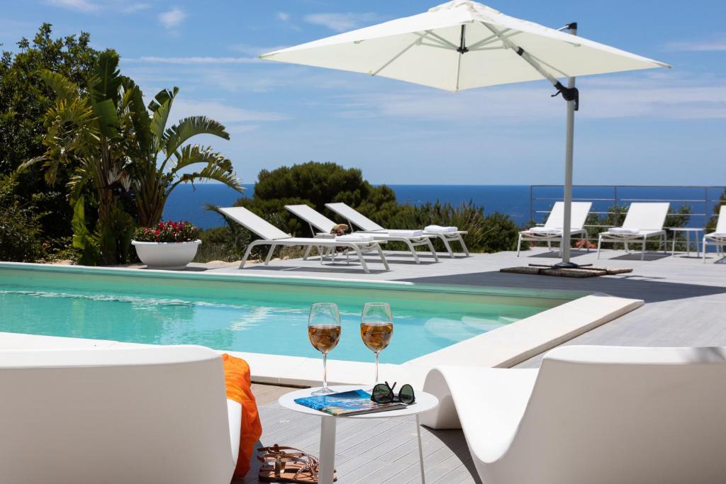 two glasses of wine sitting on a table next to a pool at Villa Annalisa by PosarelliVillas in Pizzolungo