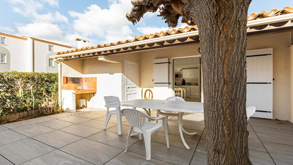 une table et des chaises sur une terrasse avec un arbre dans l'établissement Perles du Soleil- 50- Maison mezzanine- 6 pers, au Cap d'Agde