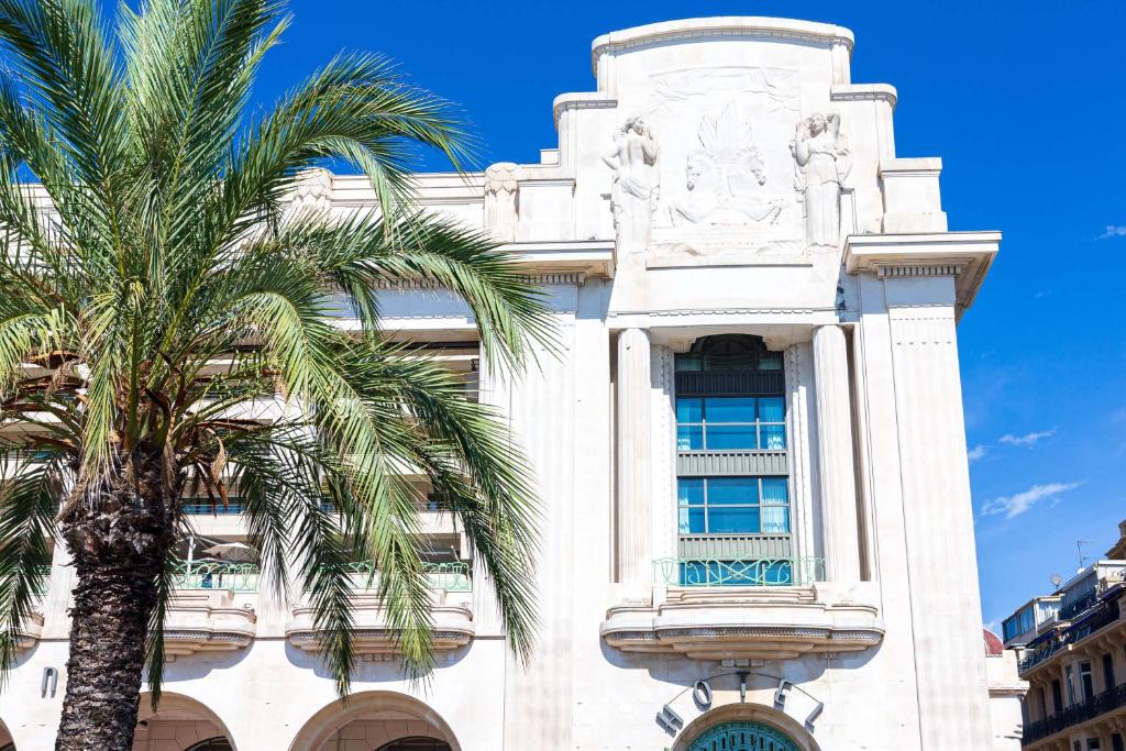 a white building with a palm tree in front of it at Hyatt Regency Nice Palais de la Méditerranée in Nice