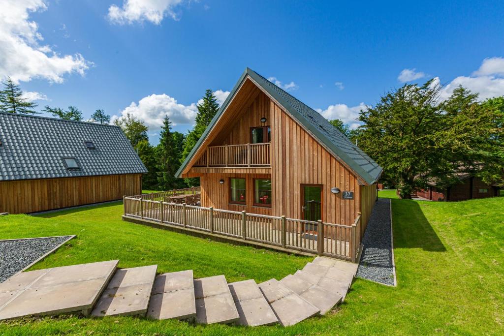 a large wooden house with a deck on a lawn at Lord Galloway 37 with Hot Tub in Newton Stewart