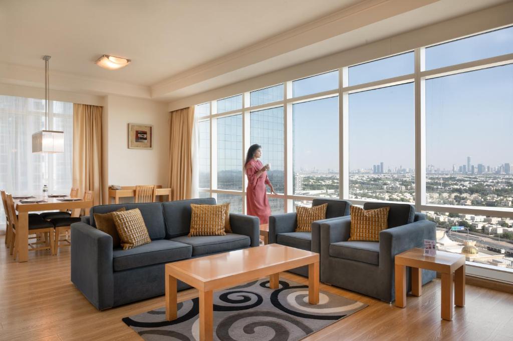 a woman standing in a living room with a large window at Oaks Liwa Heights Hotel Suites in Dubai