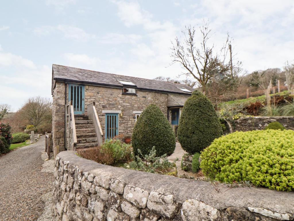 a stone house with a stone wall and bushes at The Barley Crush in Bodmin