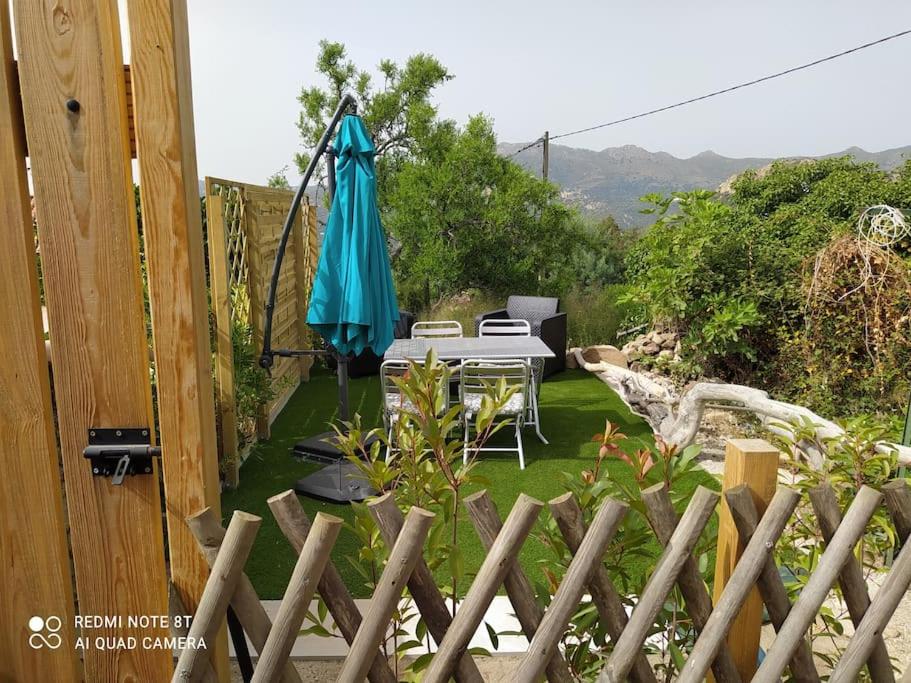 eine Terrasse mit einem Sonnenschirm, einem Tisch und Stühlen in der Unterkunft Duplex avec jardin, proche village in Calenzana