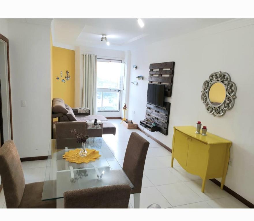 sala de estar con mesa de cristal y armario amarillo en Apartamento em Guarapari, en Guarapari