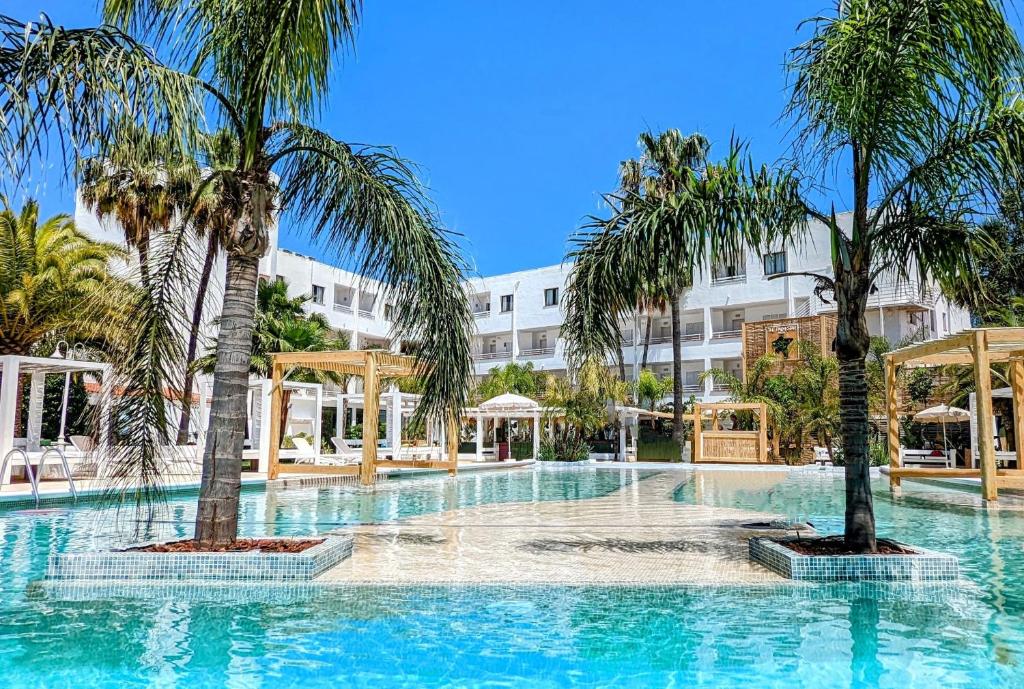- une piscine bordée de palmiers en face d'un bâtiment dans l'établissement The Palm Star Ibiza - Adults Only, à Bahía de Sant Antoni