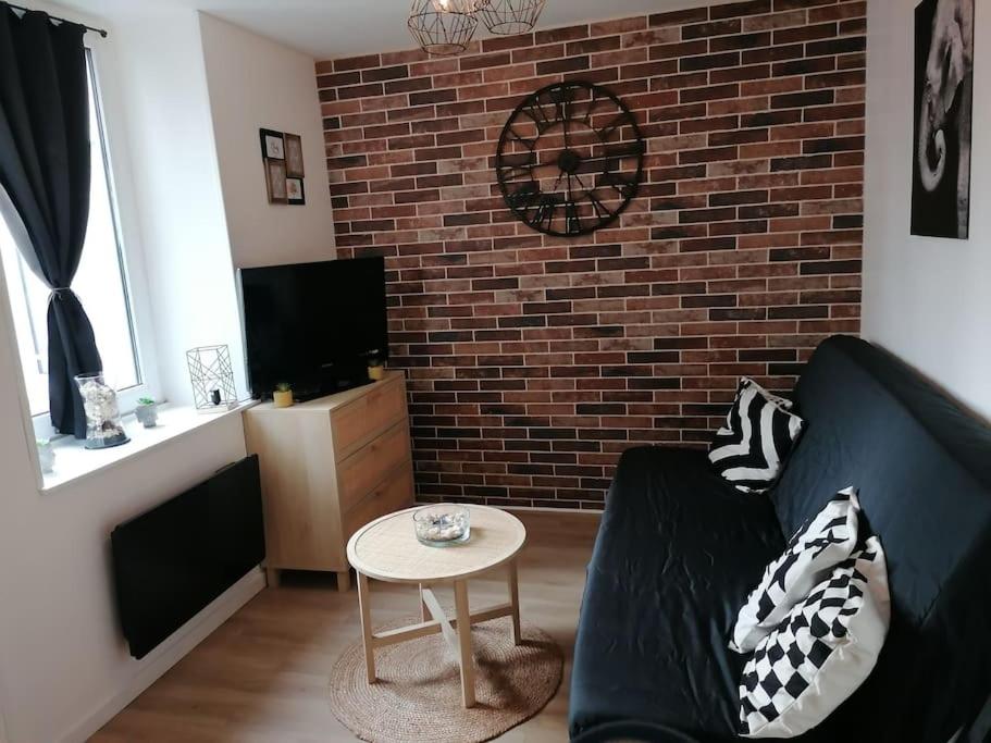 ein Wohnzimmer mit einem schwarzen Sofa und einer Ziegelwand in der Unterkunft Studio à deux pas de la mer in Berck-sur-Mer