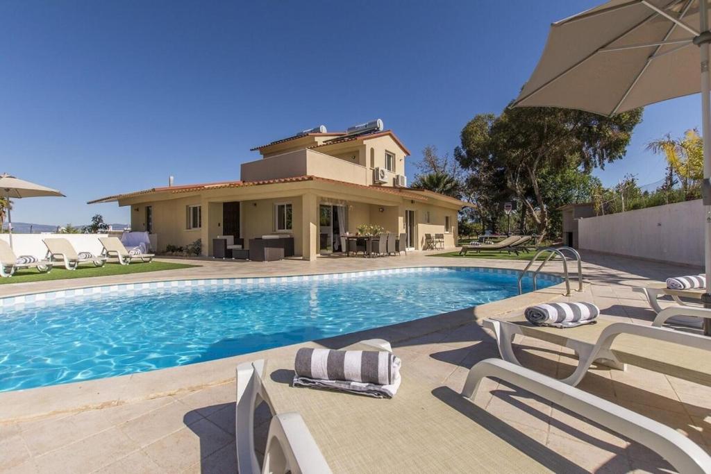 a house with a swimming pool with chairs and an umbrella at Villa Saudade in Lagoa