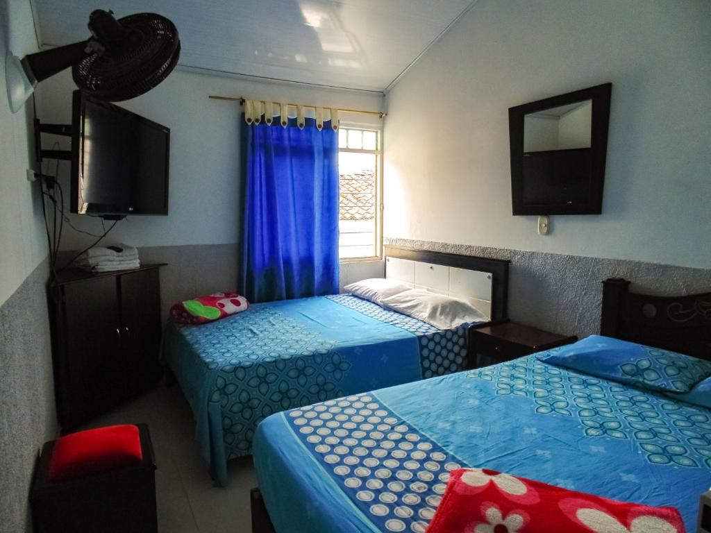 a room with two beds and a tv and a window at Hotel Ciudad Señora Buga in Buga