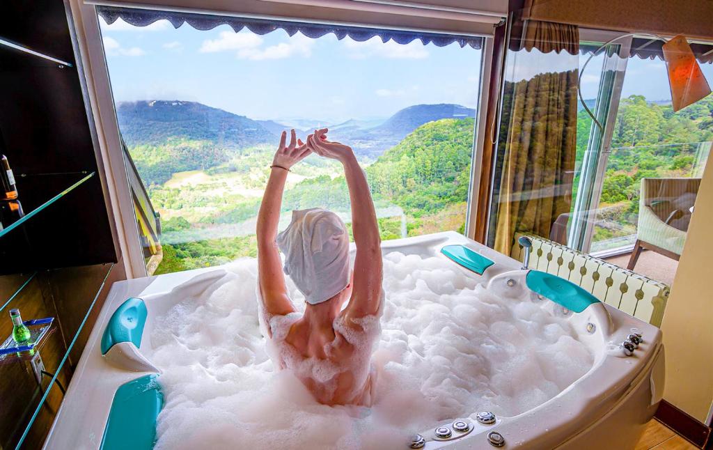 um homem numa banheira num quarto com uma janela em Villa Bella Hotel & SPA Gramado em Gramado